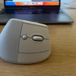 Chuột không dây Logitech Lift được đặt gần laptop trên bàn làm việc, làm nổi bật thiết kế tiện dụng.