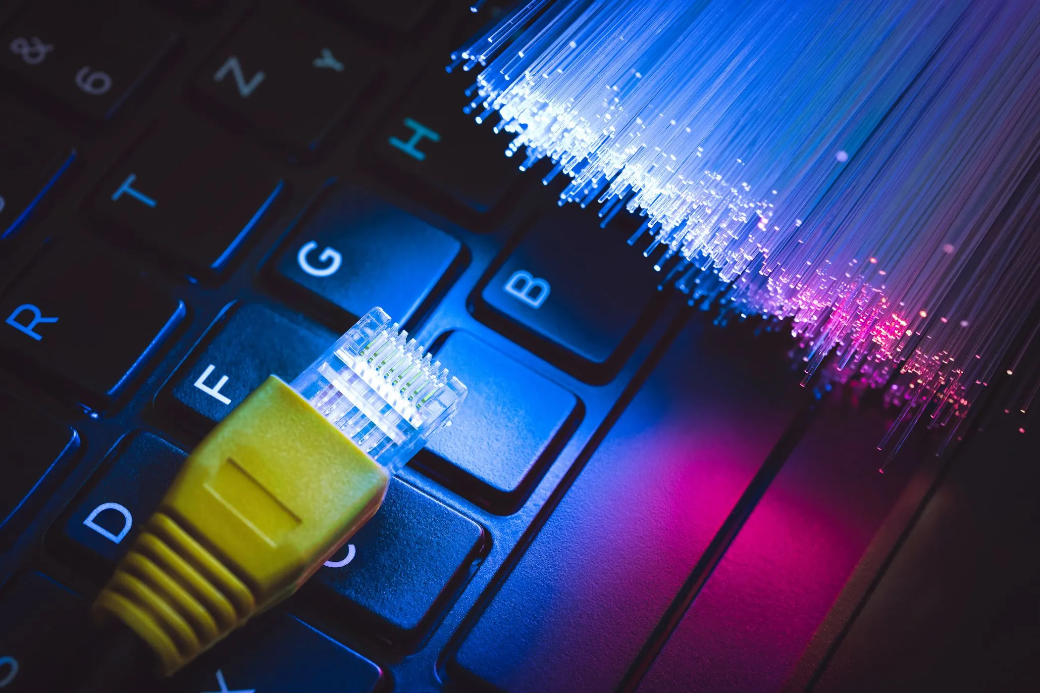 Đầu nối cáp Ethernet và cáp quang đặt trên bàn phím máy tính xách tay, tượng trưng cho việc nâng cấp băng thông internet để đảm bảo kết nối Wi-Fi ổn định và tốc độ cao