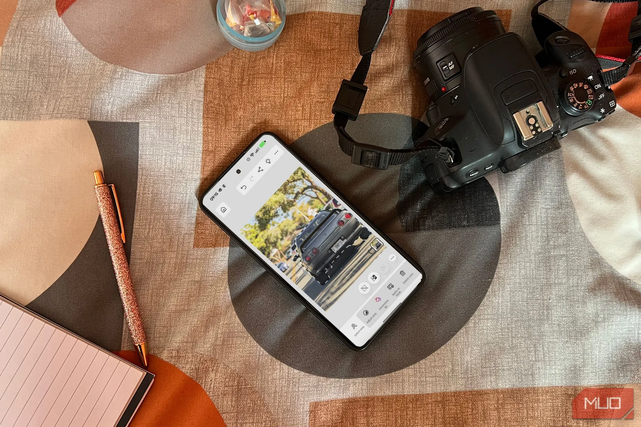Điện thoại Android hiển thị ứng dụng Photoshop trên giường cạnh máy ảnh và sổ tay