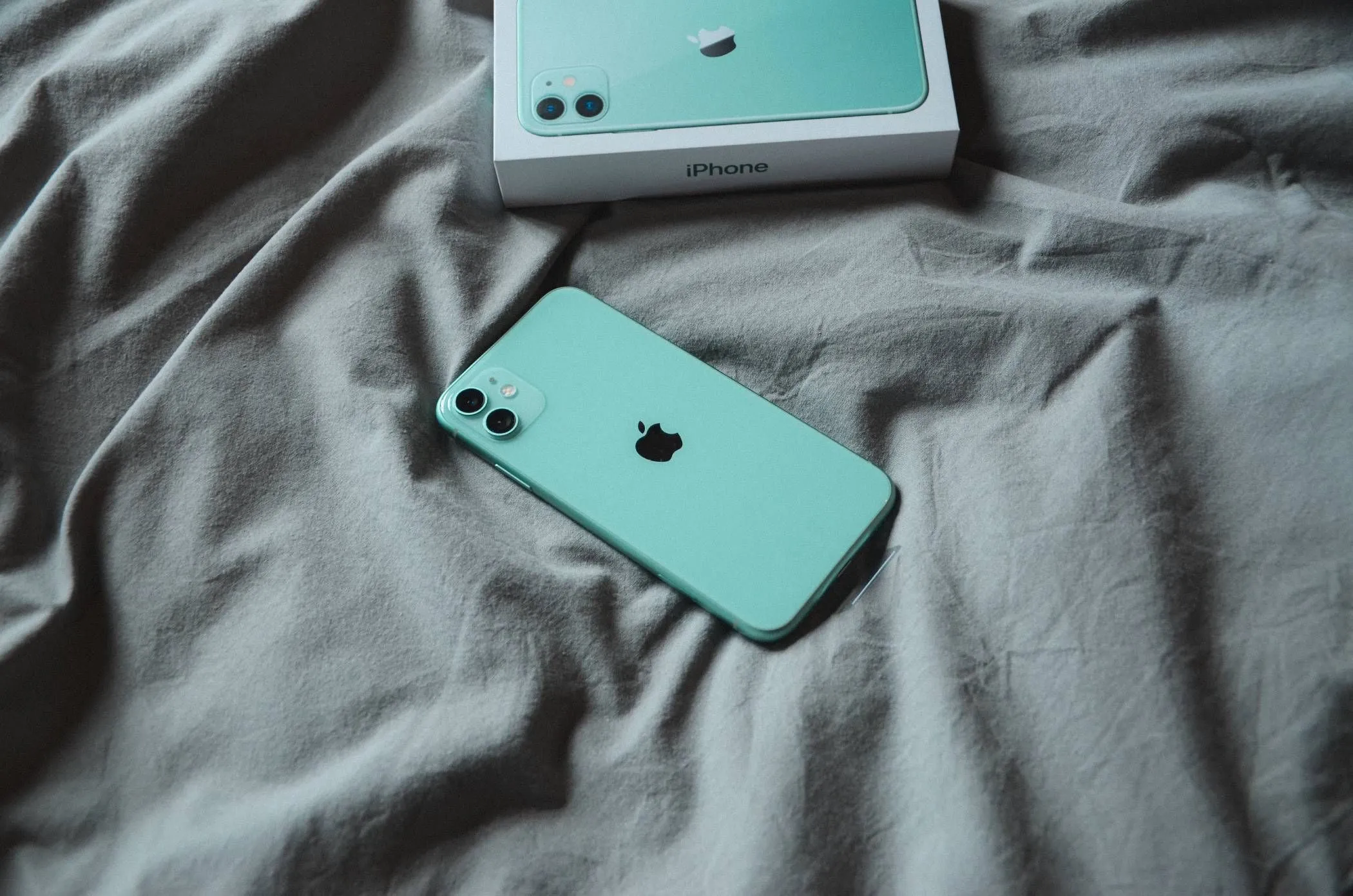 Điện thoại iPhone màu xanh lá cây đặt trên chăn hoặc ga trải giường, cảnh báo nguy cơ quá nhiệt khi sạc