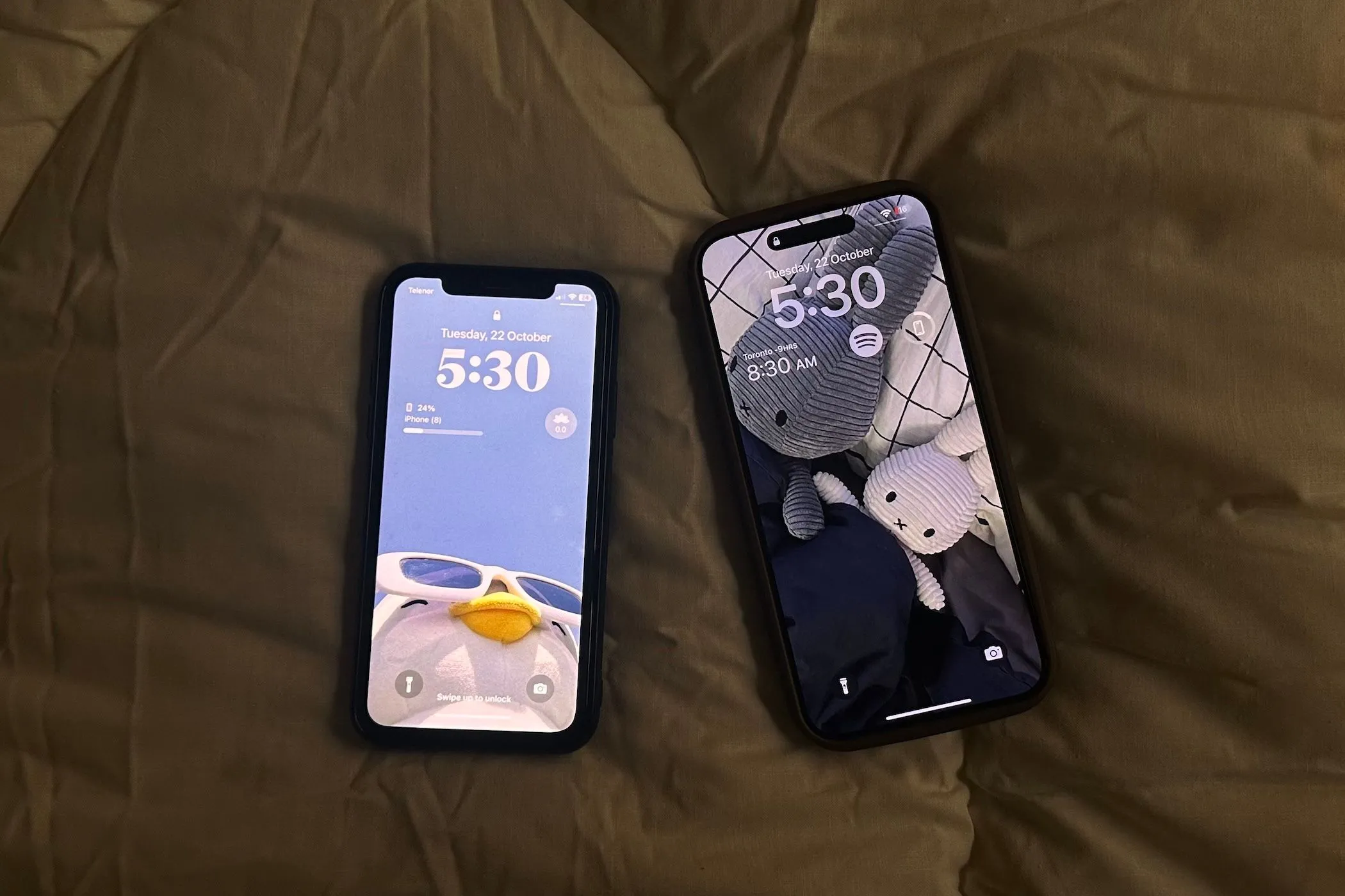 Hai chiếc điện thoại iPhone X màu đen và iPhone 15 Pro Max màu titan nằm cạnh nhau trên ga trải giường trắng, thể hiện sự so sánh giữa các dòng smartphone.