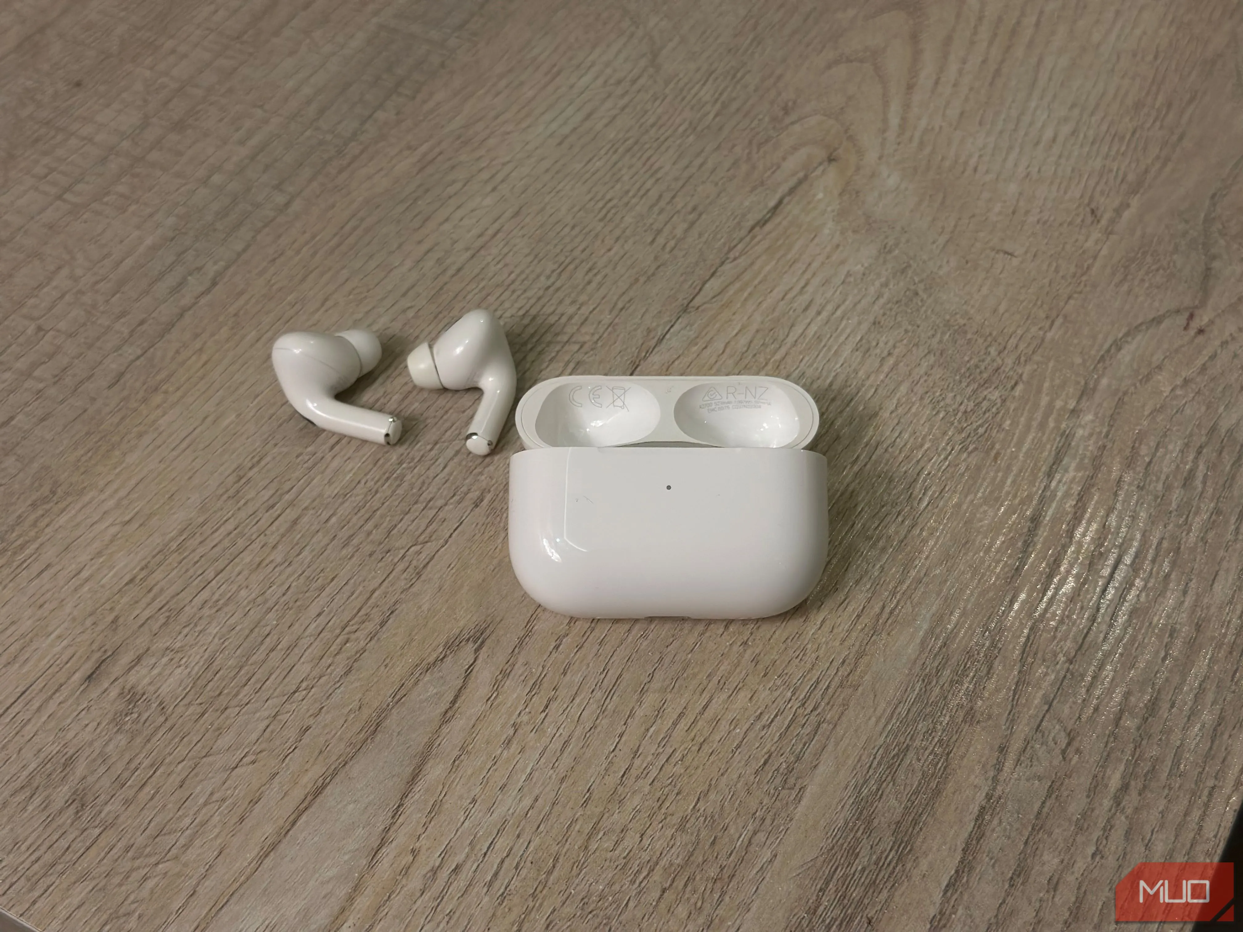 Hộp sạc AirPods và tai nghe nằm trên bàn, minh họa vị trí tìm số model và số serial dưới nắp