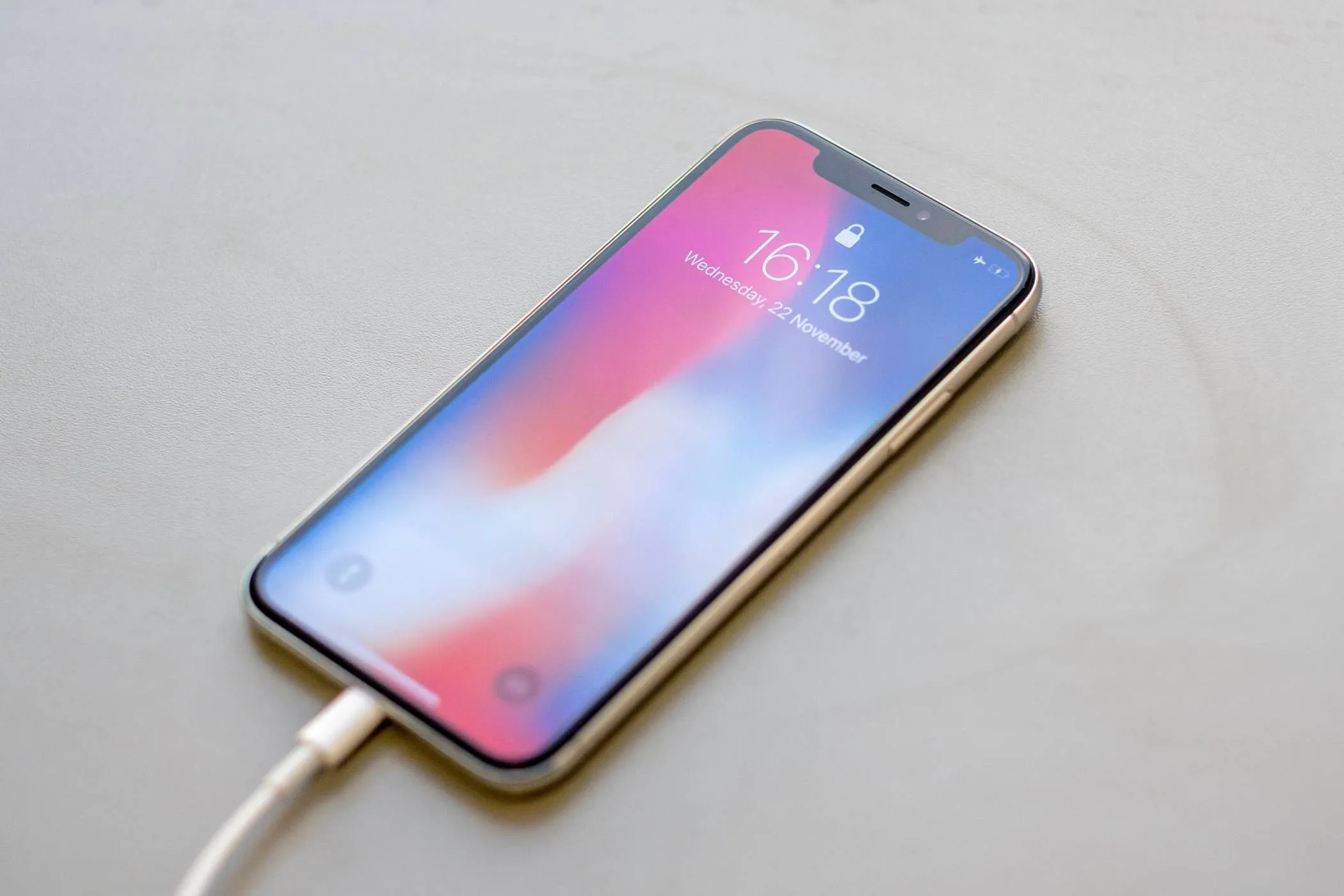 iPhone đang được cắm sạc qua cáp Lightning trên mặt bàn, thể hiện trạng thái sạc pin