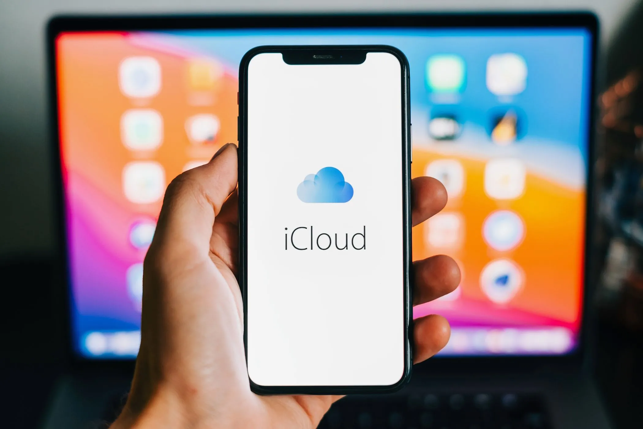 Logo iCloud trên màn hình iPhone, phía sau là MacBook, biểu tượng cho dịch vụ đám mây Apple