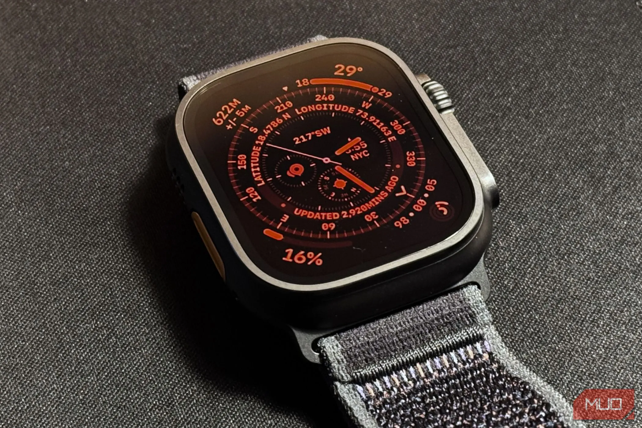 Màn hình Apple Watch Ultra 2 hiển thị mặt đồng hồ với chế độ ban đêm màu đỏ kích hoạt, đặt trên nền vật liệu màu tối.