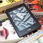 Máy đọc sách Kindle nằm trên chồng sách giấy, minh họa sự chuyển dịch từ sách in sang sách điện tử và các giới hạn mới của Amazon đối với eBook.