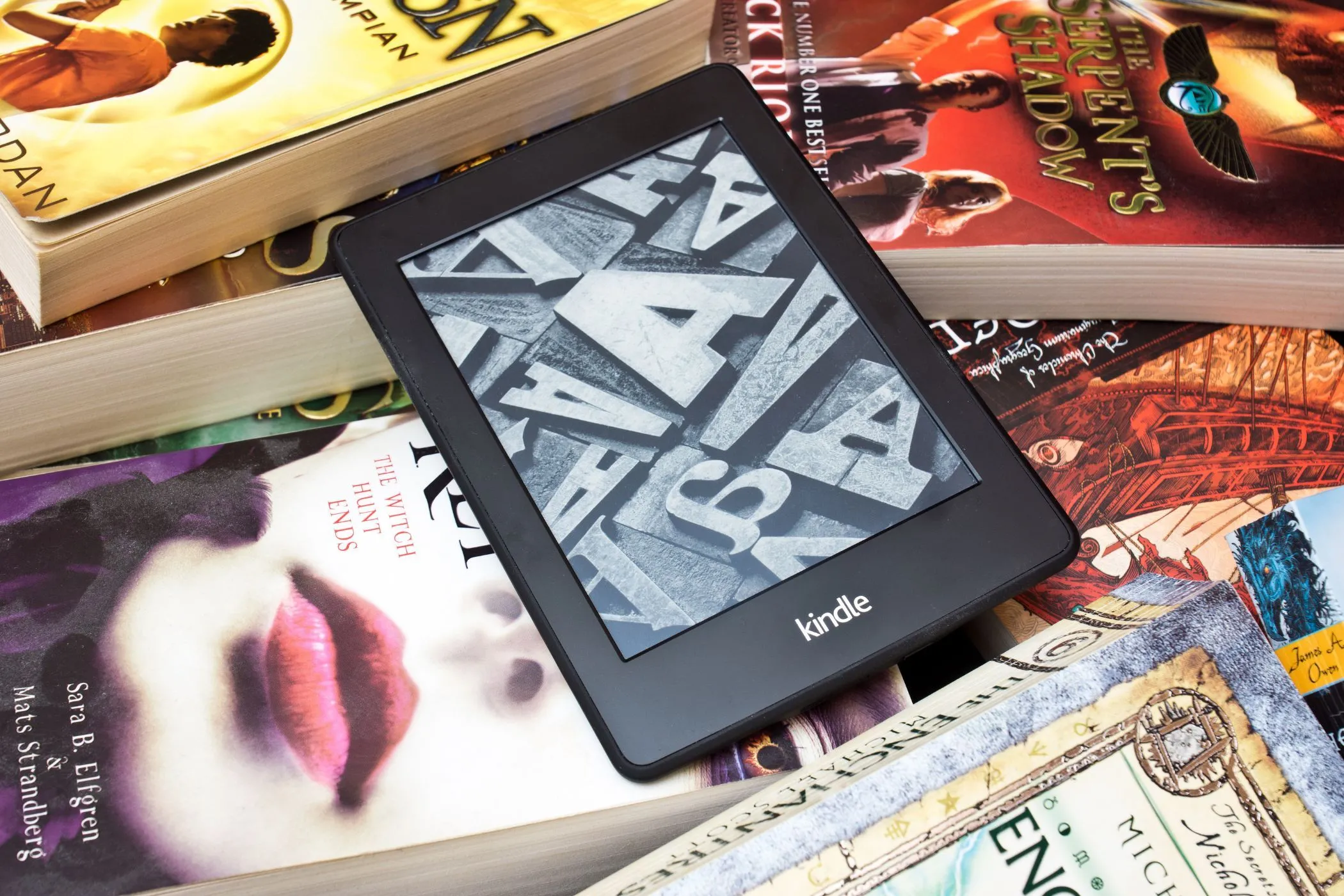 Máy đọc sách Kindle nằm trên chồng sách giấy, minh họa sự chuyển dịch từ sách in sang sách điện tử và các giới hạn mới của Amazon đối với eBook.