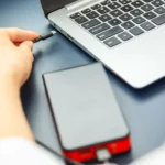 Một người phụ nữ đang cắm cáp USB-C vào laptop, minh họa việc kết nối thiết bị ngoại vi có thể làm chậm quá trình sạc.