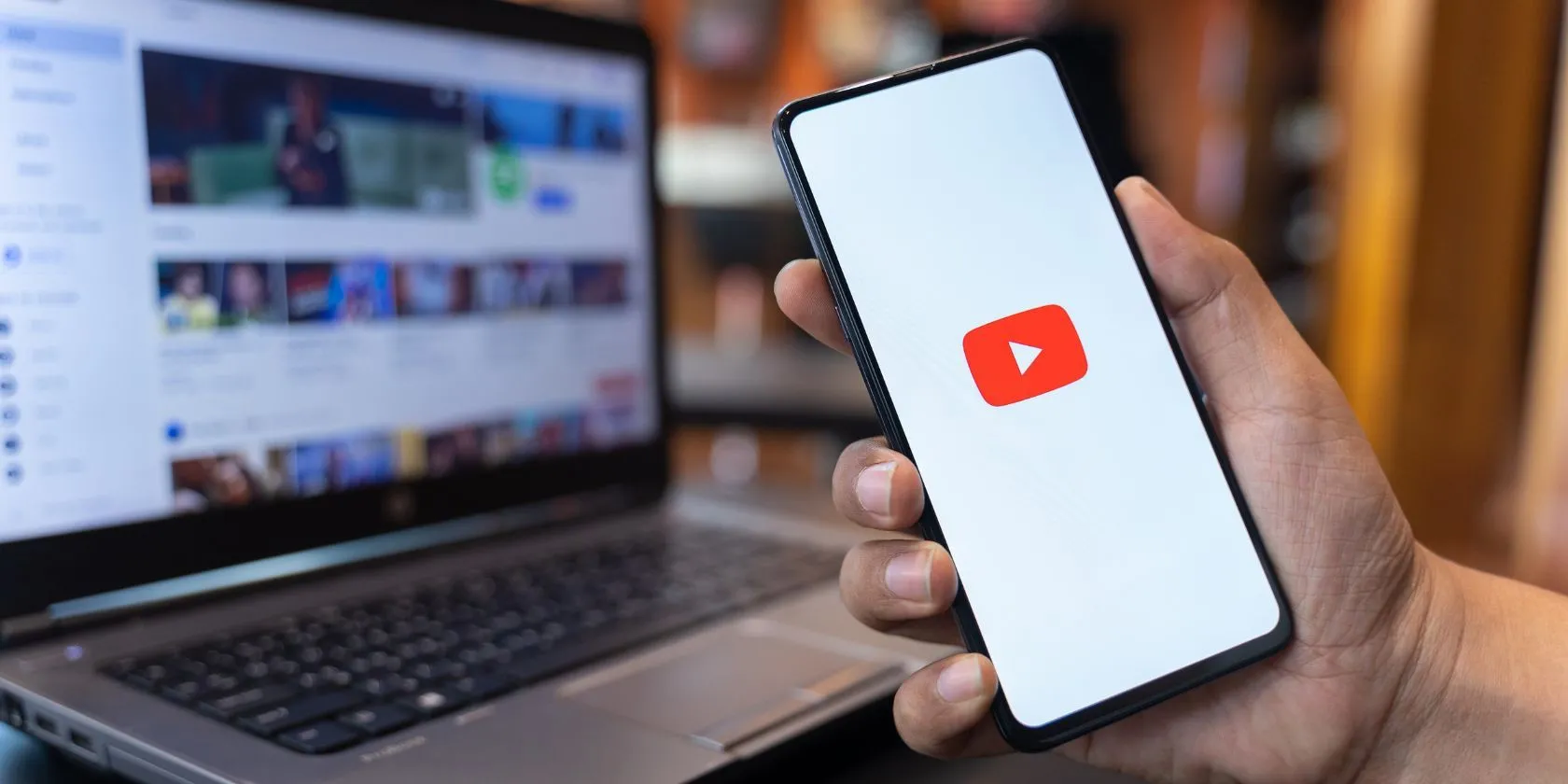 Người dùng đang thao tác trên ứng dụng YouTube trên điện thoại, phía sau là giao diện website YouTube.