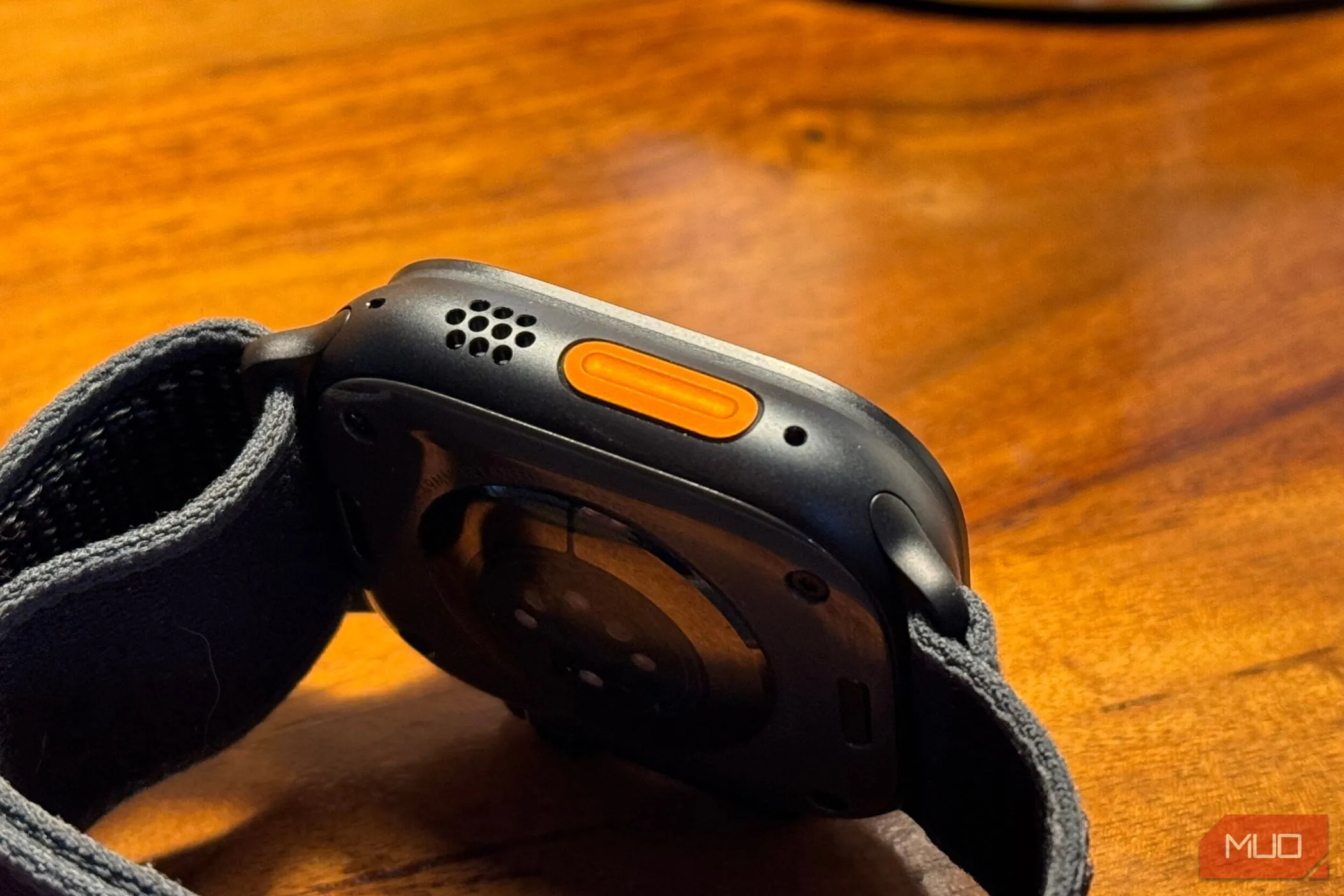 Nút Hành động màu cam nổi bật trên thân Apple Watch Ultra 2 màu titan đen, đặt trên mặt bàn.